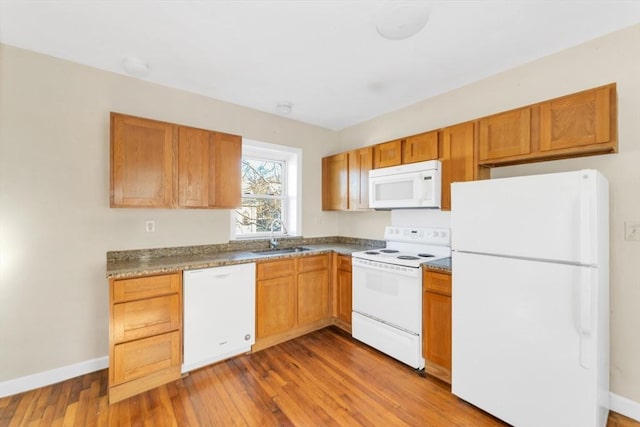 kitchen featuring baseboards, white appliances, brown cabinetry, hardwood / wood-style floors, and a sink