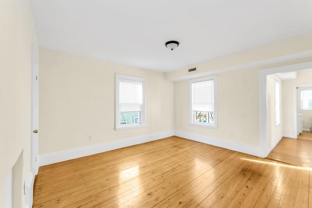 empty room featuring light wood-style floors, baseboards, visible vents, and radiator
