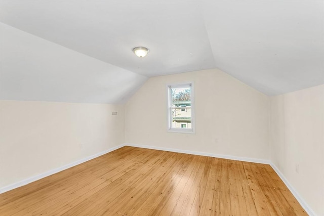 additional living space with baseboards, light wood-type flooring, and vaulted ceiling