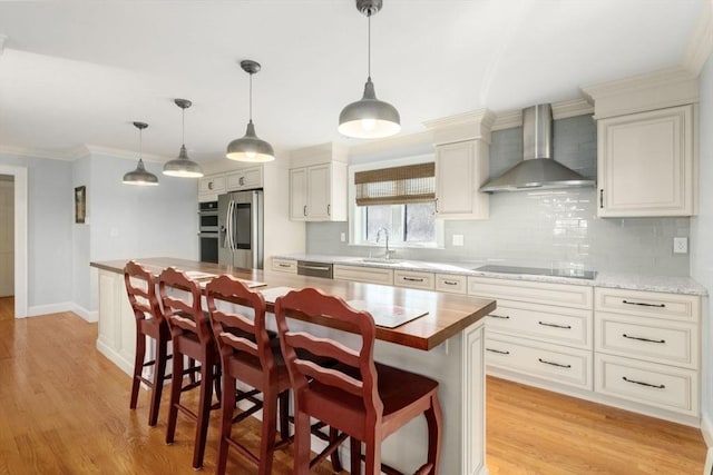 kitchen featuring wall chimney exhaust hood, a breakfast bar, hanging light fixtures, appliances with stainless steel finishes, and a kitchen island