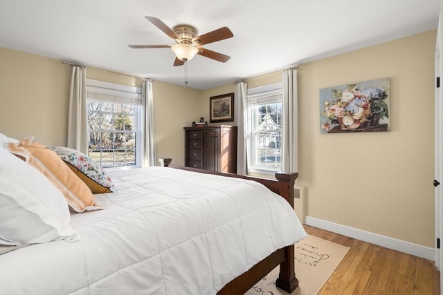 bedroom featuring multiple windows, wood-type flooring, radiator, and ceiling fan