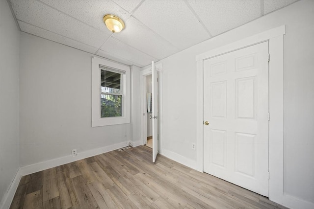 unfurnished bedroom featuring baseboards, light wood-type flooring, and a drop ceiling