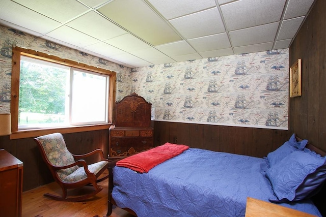 bedroom featuring a wainscoted wall, wallpapered walls, wooden walls, a paneled ceiling, and wood finished floors
