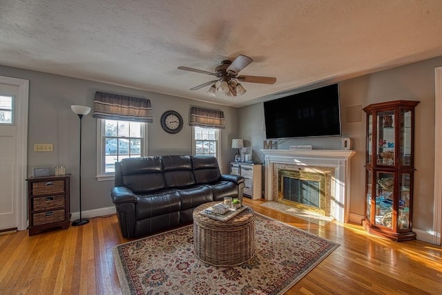 living room with a fireplace, a textured ceiling, ceiling fan, and light wood-type flooring