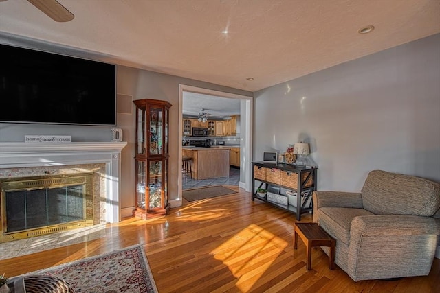 living room featuring ceiling fan, a premium fireplace, and light wood-type flooring