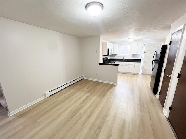 kitchen featuring freestanding refrigerator, dark countertops, light wood-style floors, a baseboard heating unit, and white cabinets