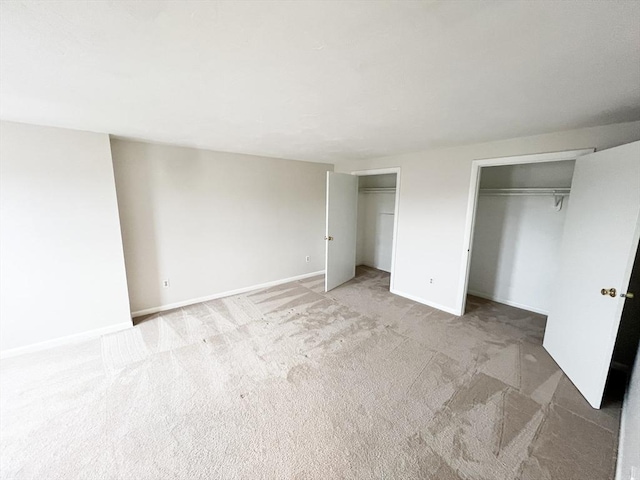 unfurnished bedroom with light colored carpet, multiple closets, and baseboards