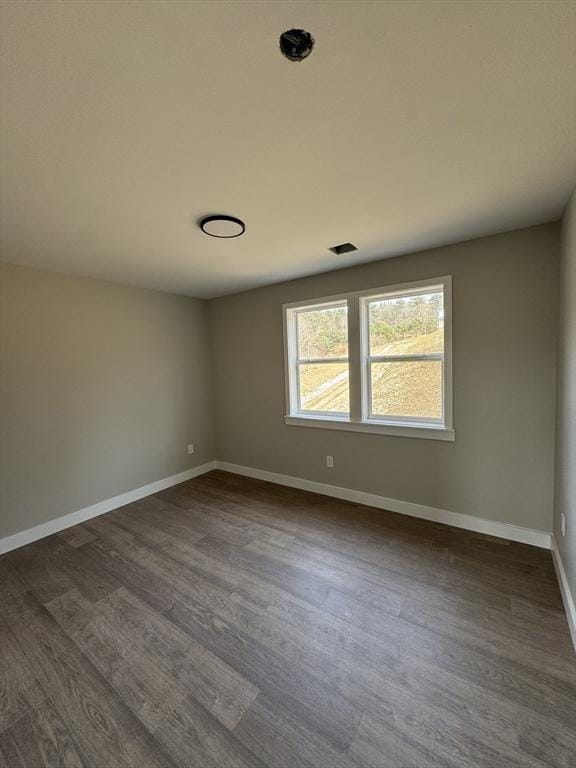 spare room with dark wood finished floors, visible vents, and baseboards