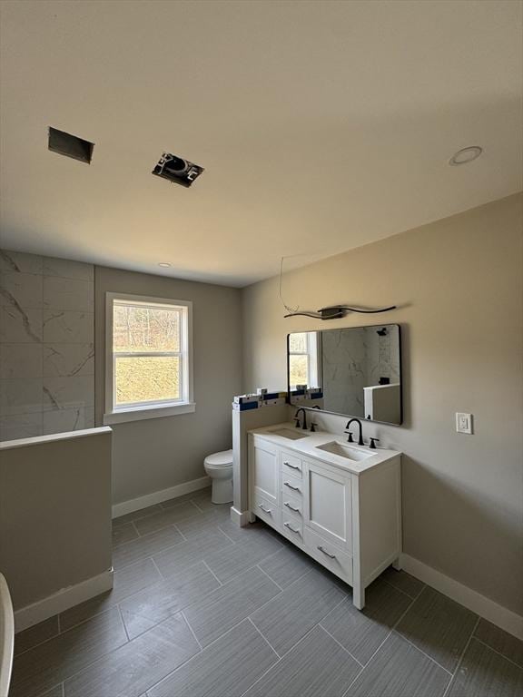 full bath with a wealth of natural light, double vanity, toilet, and a sink