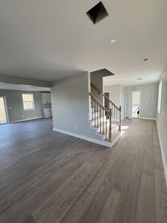 empty room featuring baseboards, dark wood-style flooring, and stairs