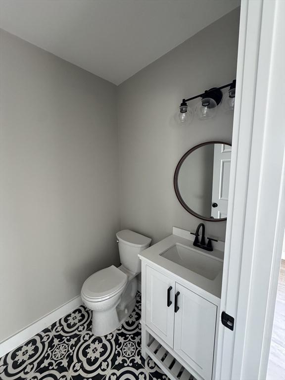 half bathroom with vanity, tile patterned floors, toilet, and baseboards