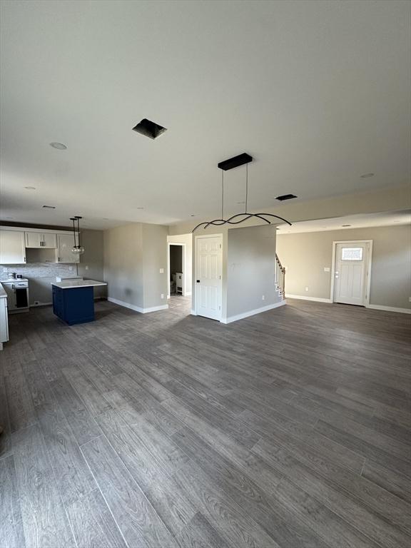 unfurnished living room with visible vents, stairway, dark wood-type flooring, and baseboards