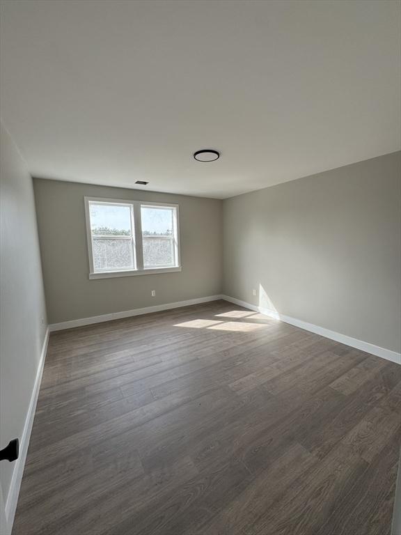 spare room featuring dark wood-style floors and baseboards