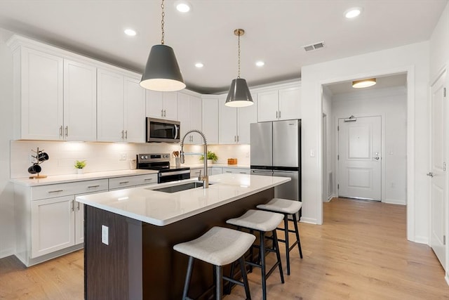 kitchen featuring white cabinetry, a center island with sink, appliances with stainless steel finishes, decorative light fixtures, and sink