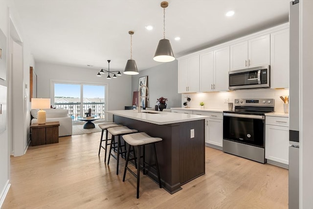 kitchen with white cabinetry, a center island with sink, stainless steel appliances, and hanging light fixtures