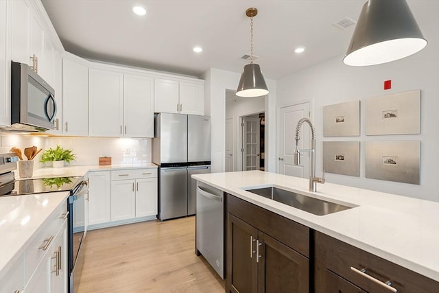 kitchen with stainless steel appliances, pendant lighting, white cabinetry, and sink