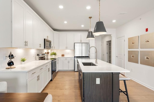 kitchen with pendant lighting, sink, appliances with stainless steel finishes, an island with sink, and white cabinets