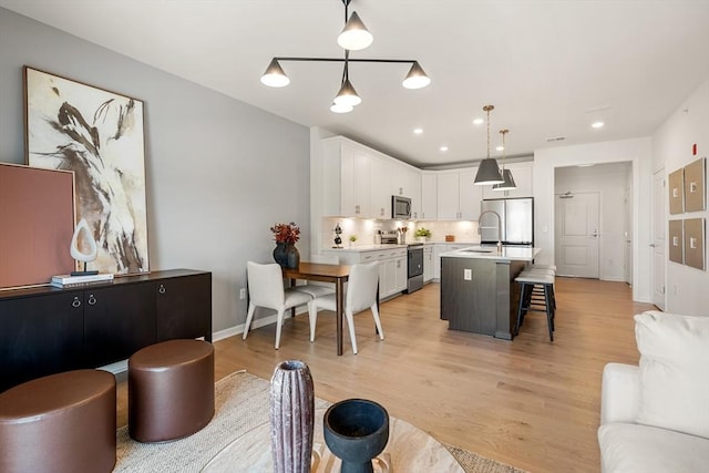 interior space featuring pendant lighting, white cabinets, appliances with stainless steel finishes, a kitchen bar, and a center island with sink