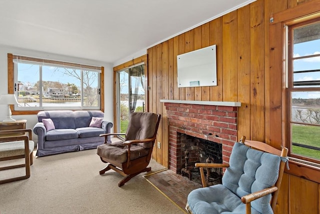 living area featuring a brick fireplace, wooden walls, carpet floors, and plenty of natural light