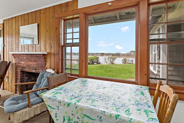 dining area with wood walls, a fireplace, crown molding, and a water view