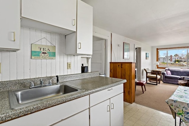 kitchen featuring white cabinetry, light carpet, open floor plan, and a sink