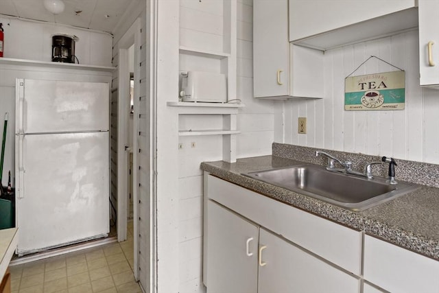 kitchen with white cabinetry, dark countertops, a sink, and freestanding refrigerator