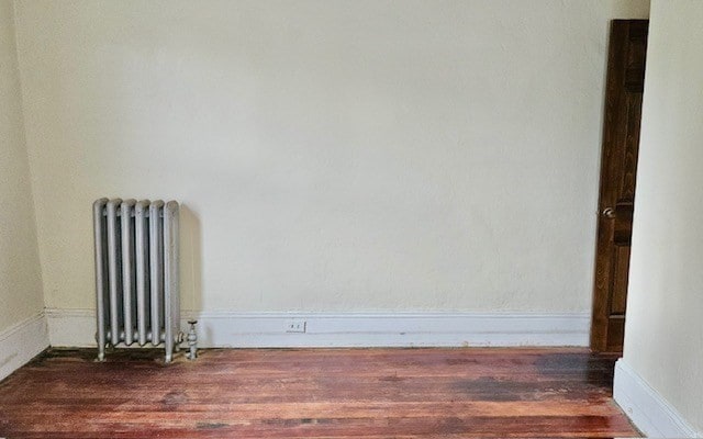 empty room featuring dark wood-type flooring and radiator heating unit