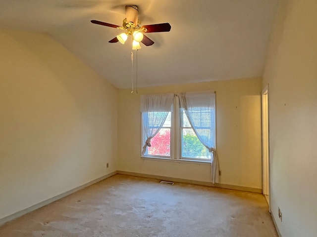 empty room featuring lofted ceiling, light colored carpet, visible vents, ceiling fan, and baseboards