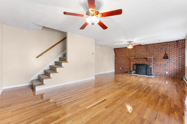 unfurnished living room featuring light wood-type flooring, a fireplace, brick wall, and ceiling fan