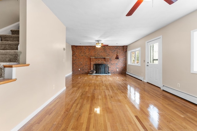 unfurnished living room featuring a baseboard radiator, hardwood / wood-style flooring, a brick fireplace, and brick wall