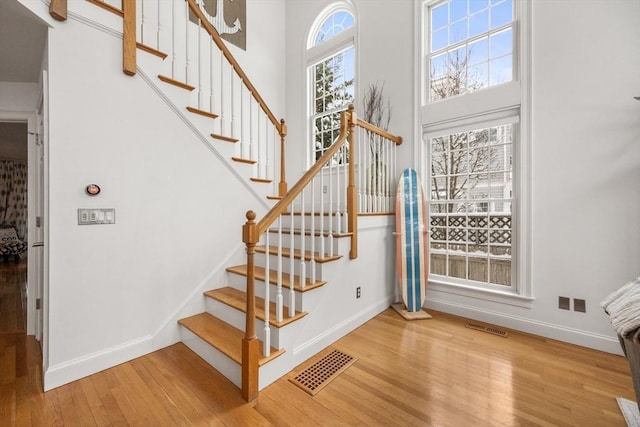 stairway featuring visible vents, baseboards, a high ceiling, and wood finished floors