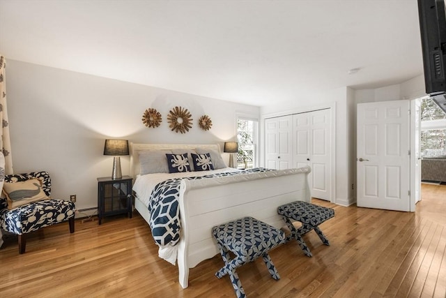 bedroom with multiple windows, light wood-style floors, a closet, and a baseboard radiator