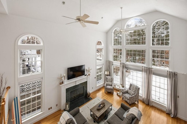 living area with a high end fireplace, ceiling fan, baseboards, lofted ceiling, and light wood-style floors