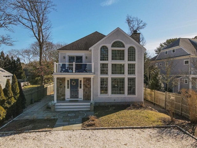 view of front of property with a chimney, a balcony, and fence