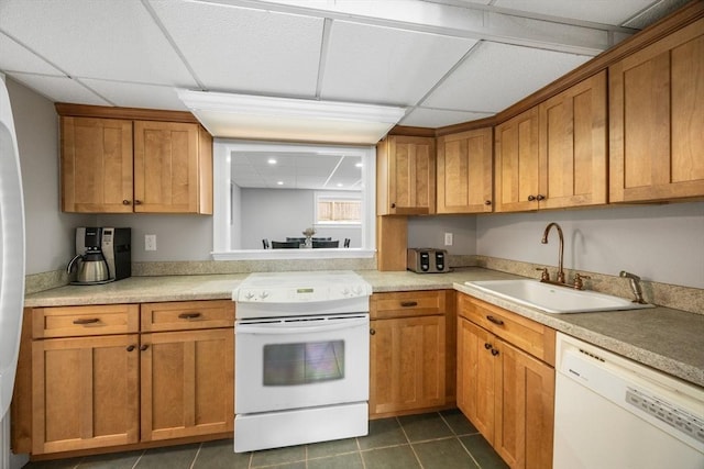 kitchen with white appliances, a drop ceiling, a sink, dark tile patterned floors, and brown cabinets