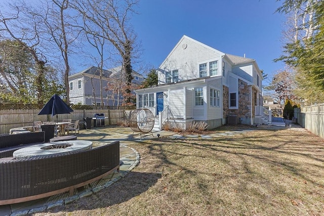 rear view of property featuring a yard, a fenced backyard, and a fire pit