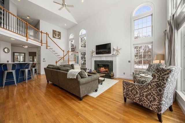 living room with stairway, light wood-style floors, a high end fireplace, and high vaulted ceiling