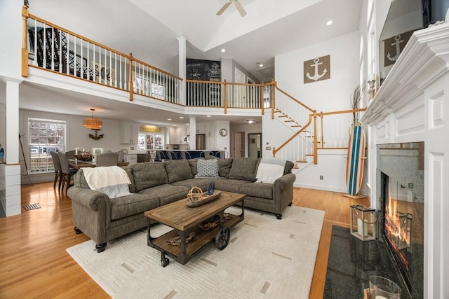 living room featuring light wood-type flooring, a fireplace with flush hearth, high vaulted ceiling, and stairway