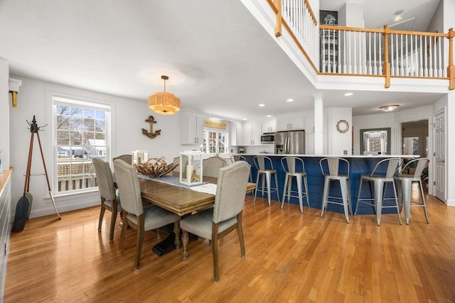 dining area featuring recessed lighting, light wood finished floors, baseboards, a towering ceiling, and ornate columns