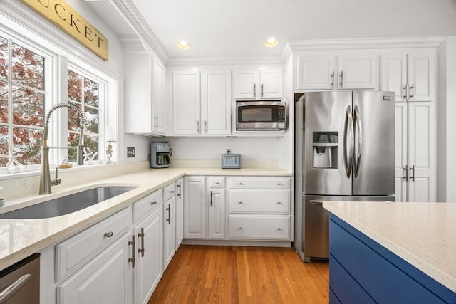 kitchen with light wood finished floors, white cabinets, stainless steel appliances, and a sink