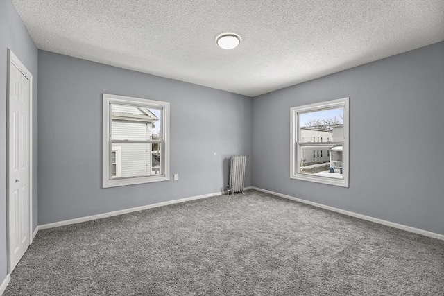 unfurnished room with radiator heating unit, a healthy amount of sunlight, carpet floors, and a textured ceiling