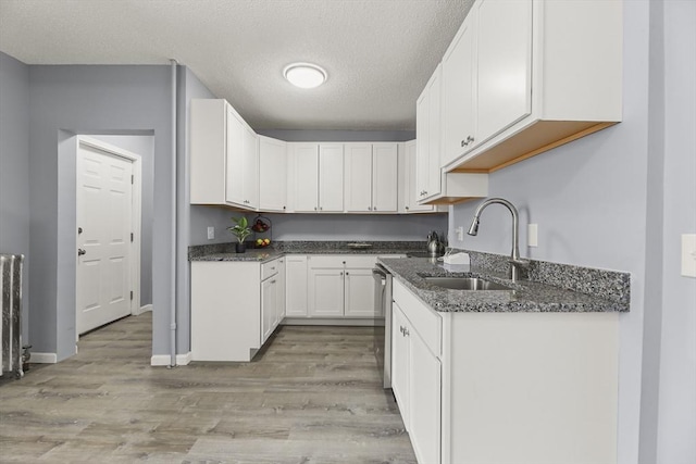 kitchen with light wood-type flooring, sink, stainless steel dishwasher, a textured ceiling, and white cabinets