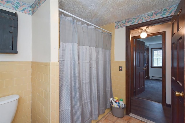 bathroom with a shower with curtain, tile walls, tile patterned flooring, a wainscoted wall, and toilet