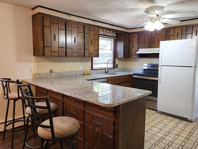 kitchen with freestanding refrigerator, a peninsula, under cabinet range hood, a sink, and stainless steel range with electric cooktop