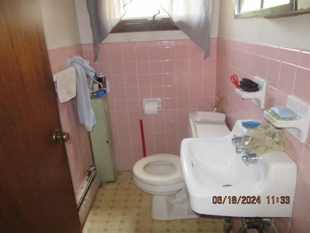 bathroom featuring toilet, tile walls, a baseboard heating unit, and sink