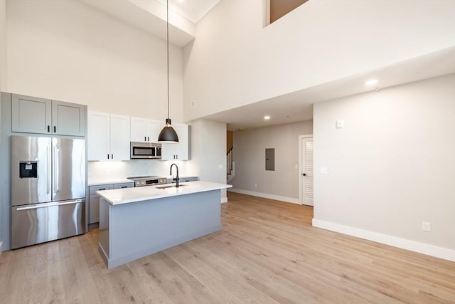 kitchen featuring decorative light fixtures, sink, stainless steel appliances, a center island with sink, and light hardwood / wood-style flooring