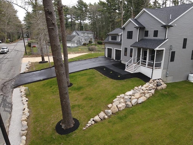 exterior space featuring a lawn, aphalt driveway, a shingled roof, and a garage