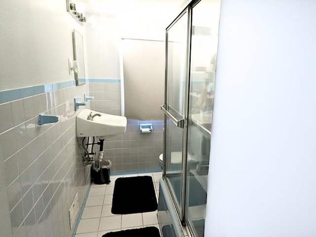 bathroom with a wainscoted wall, tile walls, toilet, an enclosed shower, and tile patterned floors