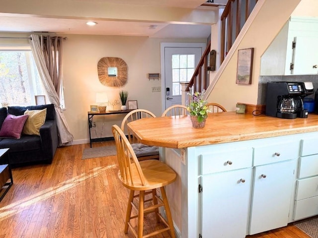 kitchen featuring light countertops, white cabinets, a kitchen breakfast bar, light wood-type flooring, and baseboards