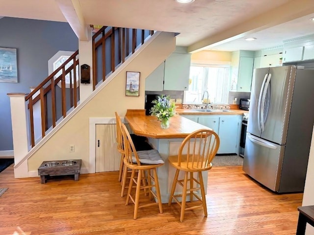 kitchen featuring light wood-style flooring, a sink, wooden counters, freestanding refrigerator, and beamed ceiling